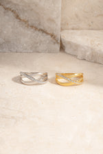Two triple band diamond rings, one silver and one gold, on a light stone surface.