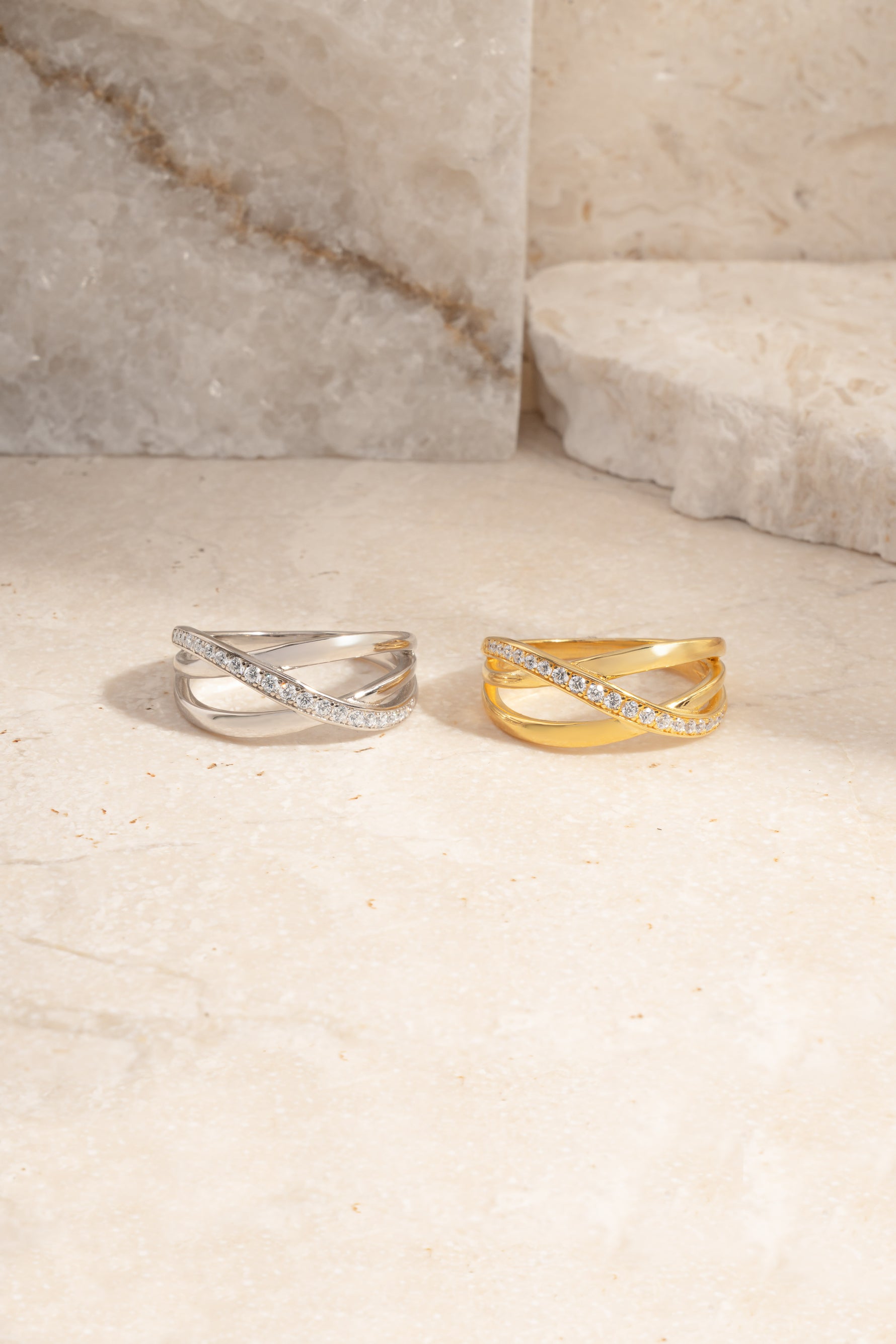 Two triple band diamond rings, one silver and one gold, on a light stone surface.