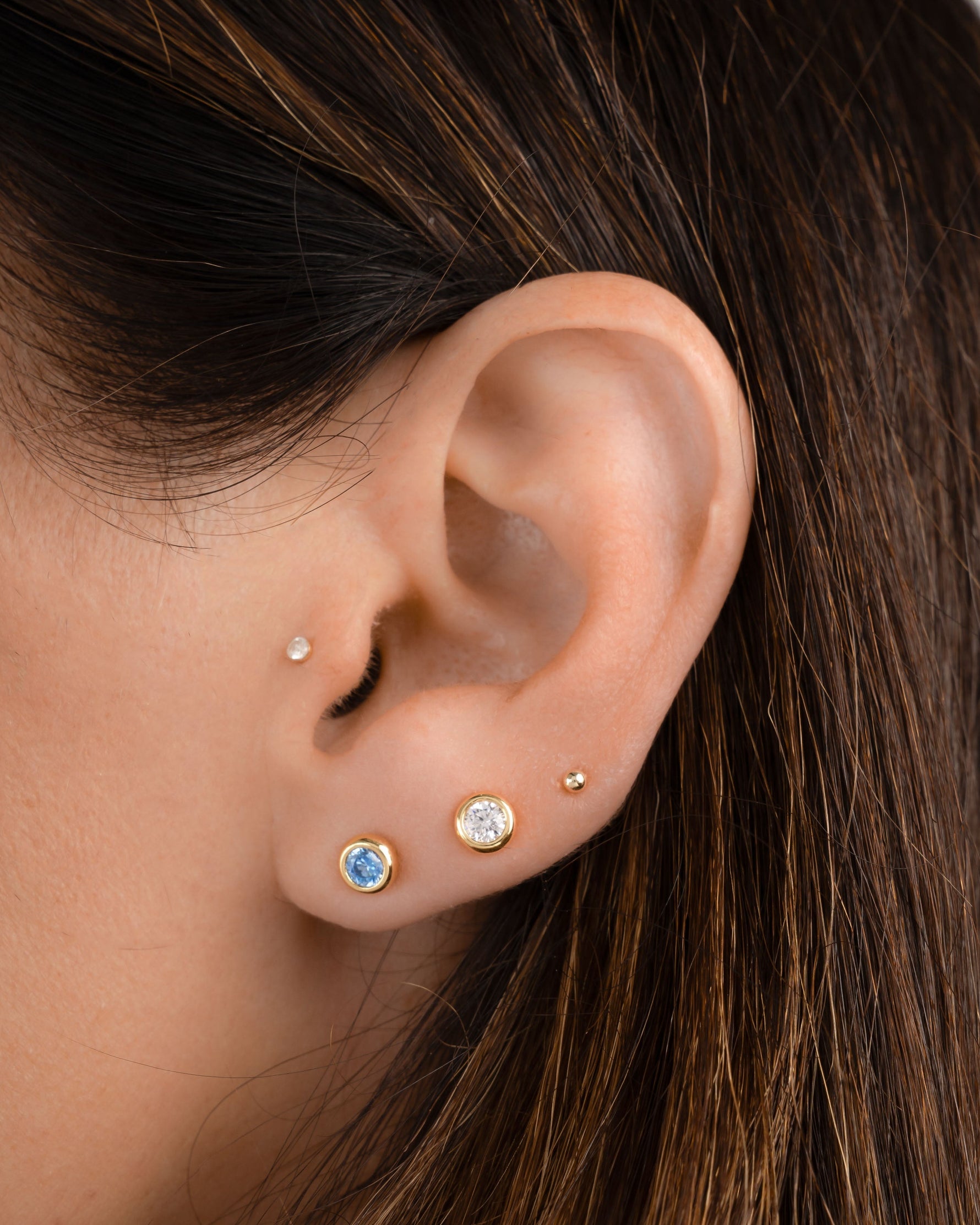 Closeup image of model wearing aquamarine earrings and diamond stud earrings with a ball stud 