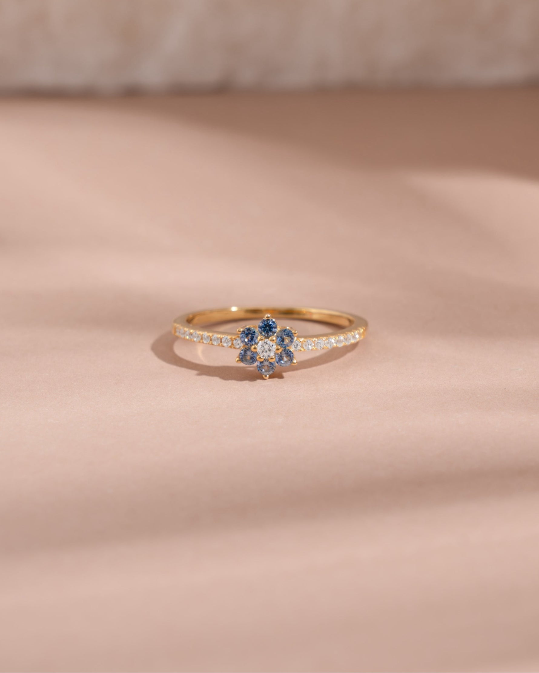 Gold minimalist ring with a blue gemstone on a beige background