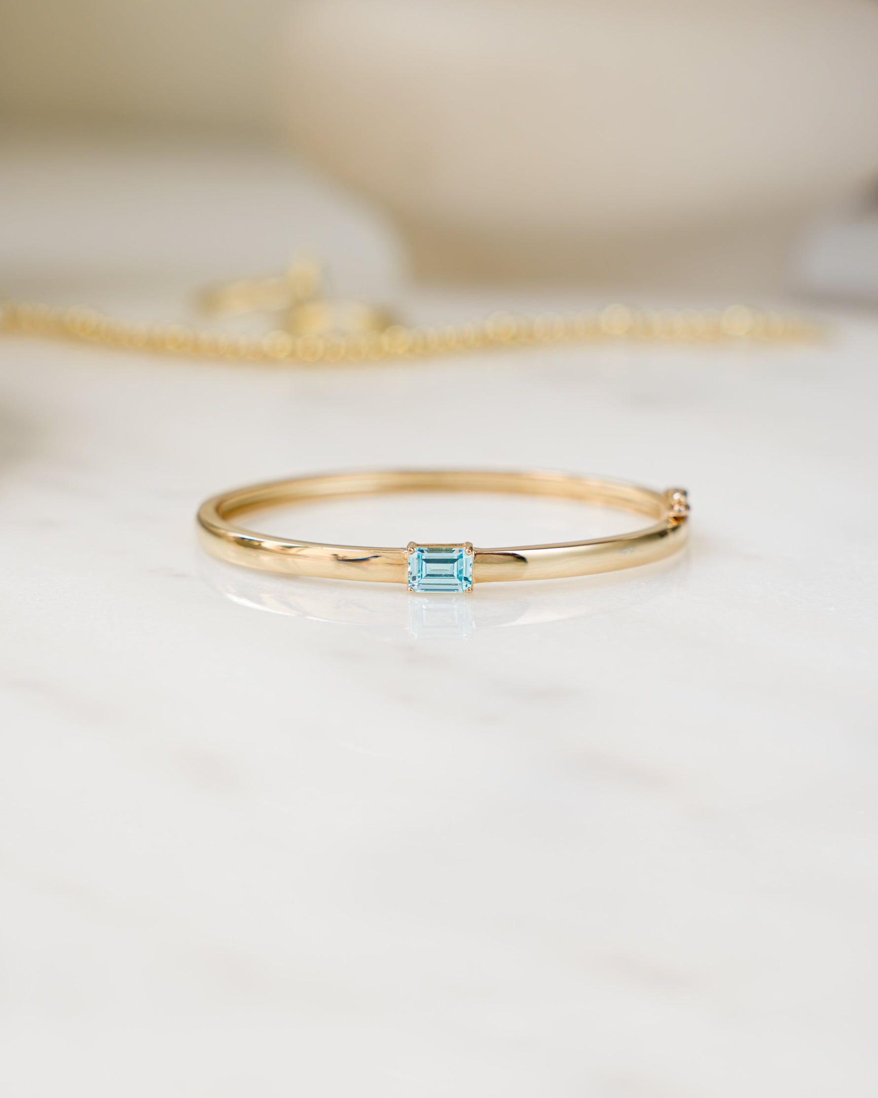 Gold bangle bracelet with a aquamarine gemstone on a white surface