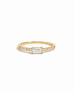 Gold ring with a central baguette diamond and smaller diamonds on a white background