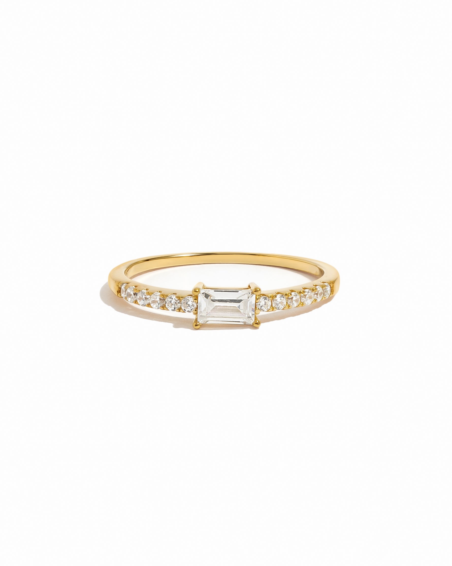 Gold ring with a central baguette diamond and smaller diamonds on a white background