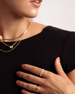 closeup image of model wearing gold jewelry featuring a gold necklace stack, an emerald ring, and a marquise eternity ring