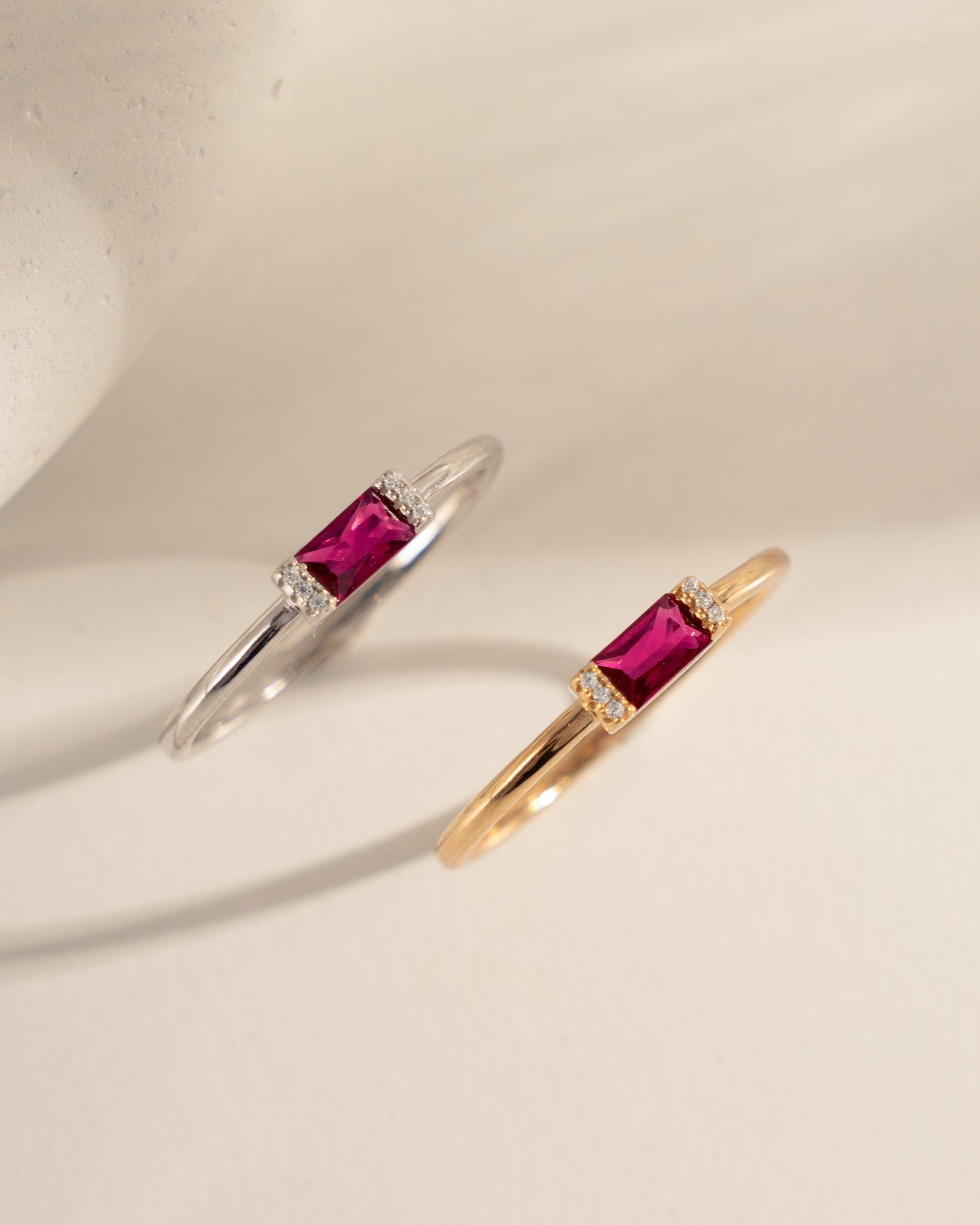 two pairs of baguette dainty rings, one in sterling silver with a ruby baguette center stone and a gold dainty ring with a ruby baguette stone