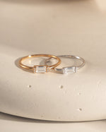 closeup image of two dainty simple baguette rings, one in gold and one in 925 sterling silver