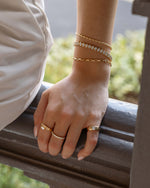 Model wearing bracelet stack featuring gold beaded bracelet, oval bezel tennis bracelet, and small paperclip bracelet
