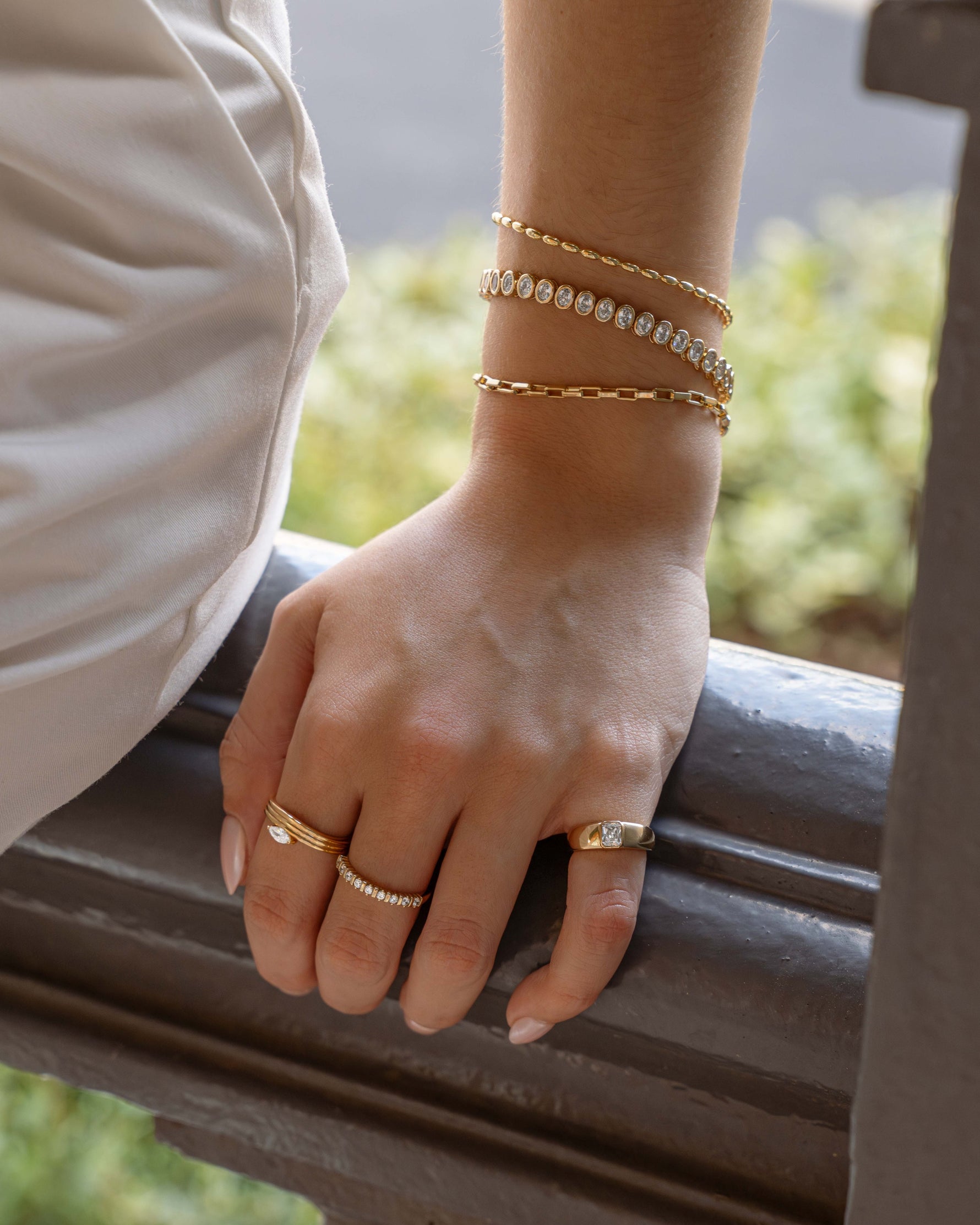 Model wearing bracelet stack featuring gold beaded bracelet, oval bezel tennis bracelet, and small paperclip bracelet
