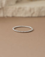 Silver plain beaded ring on a beige surface