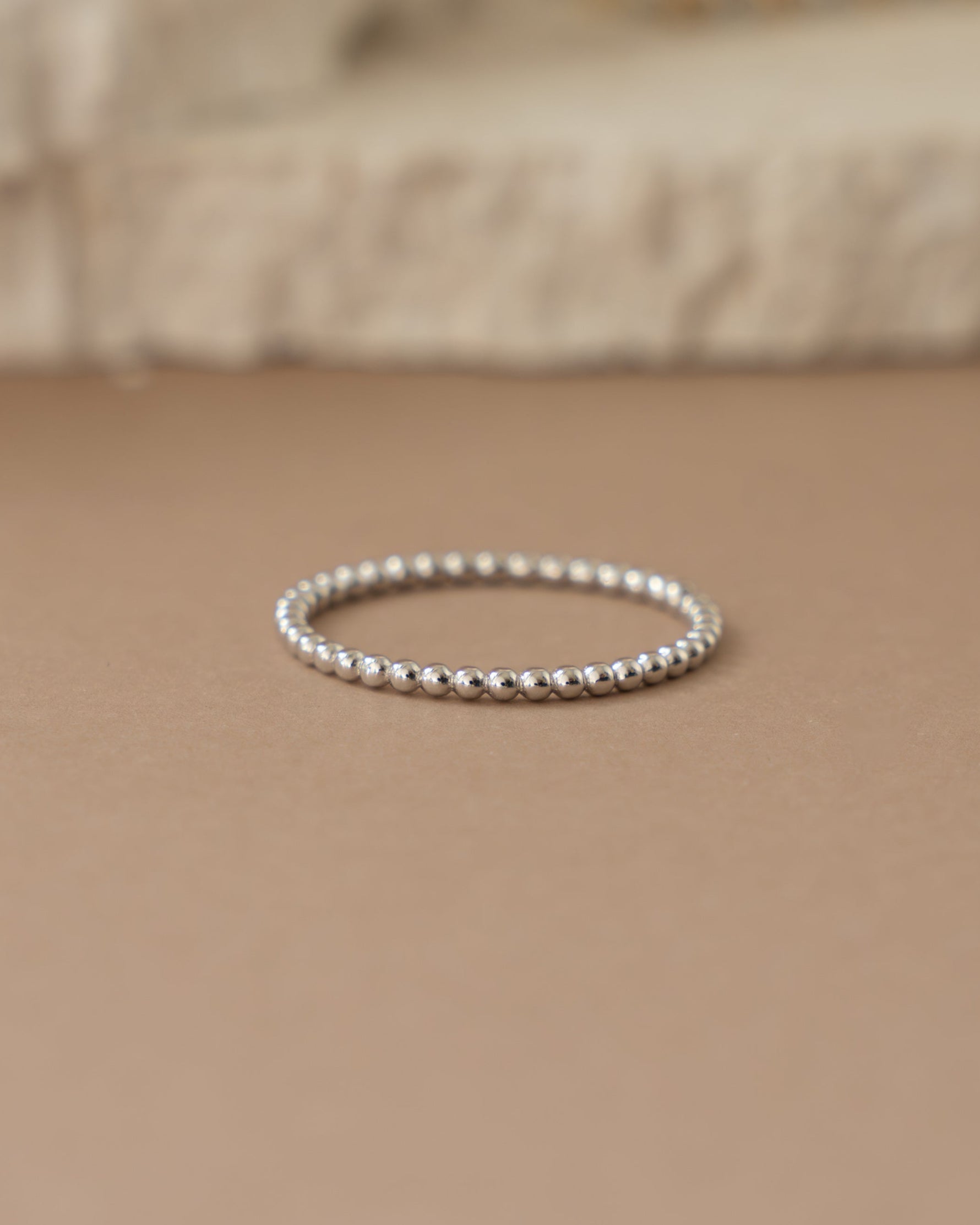 Silver plain beaded ring on a beige surface