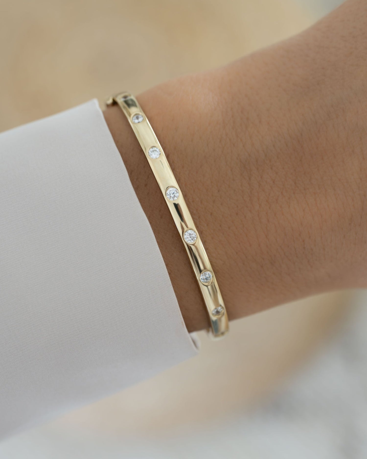 Model wearing gold bangle with small cz diamonds on a wrist against a neutral background