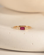 closeup image of gold dainty ring with ruby birthstone and a baguette stone