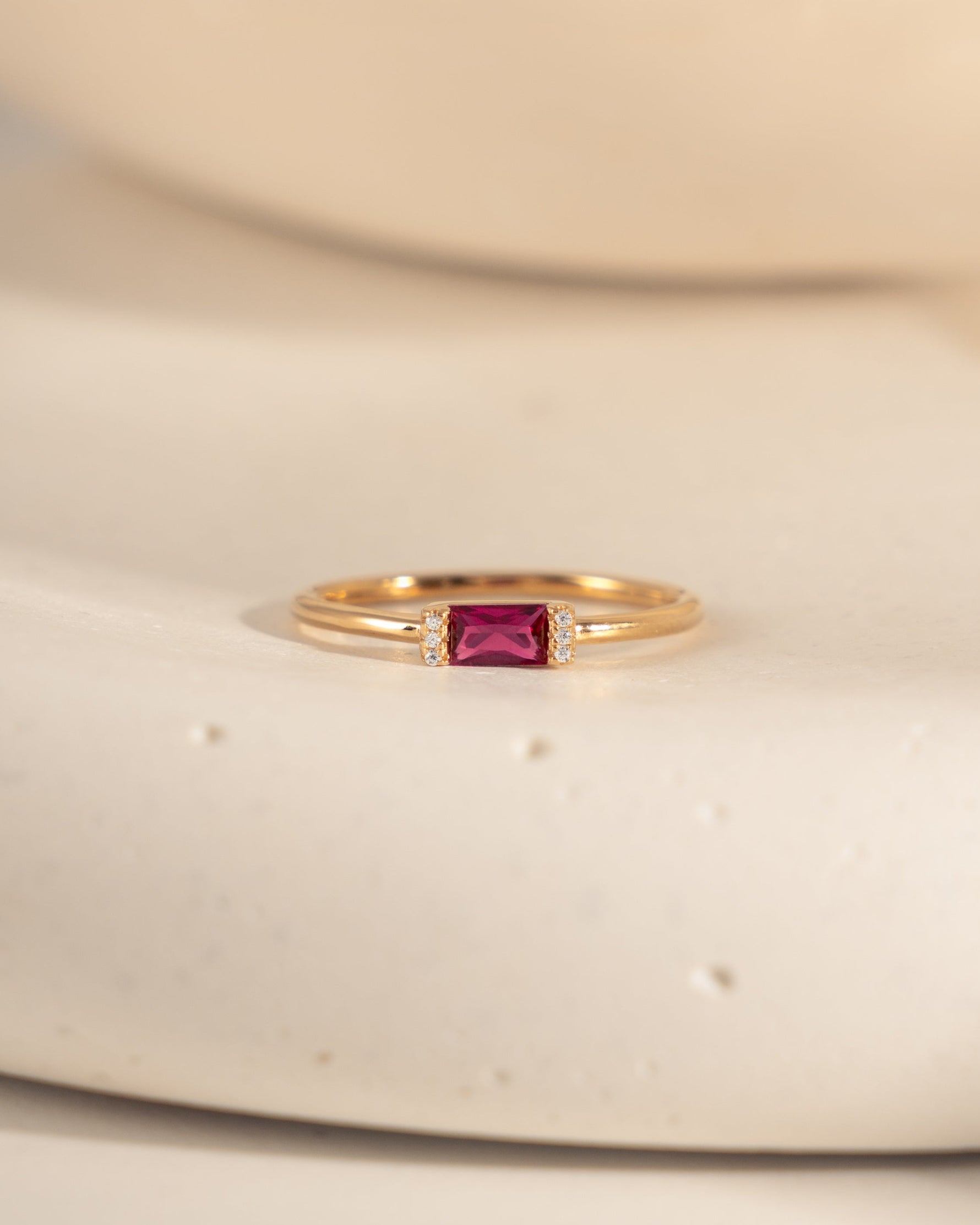 closeup image of gold dainty ring with ruby birthstone and a baguette stone
