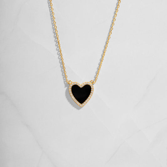 Close-up of a heart necklace with black onyx, set on a delicate gold chain 