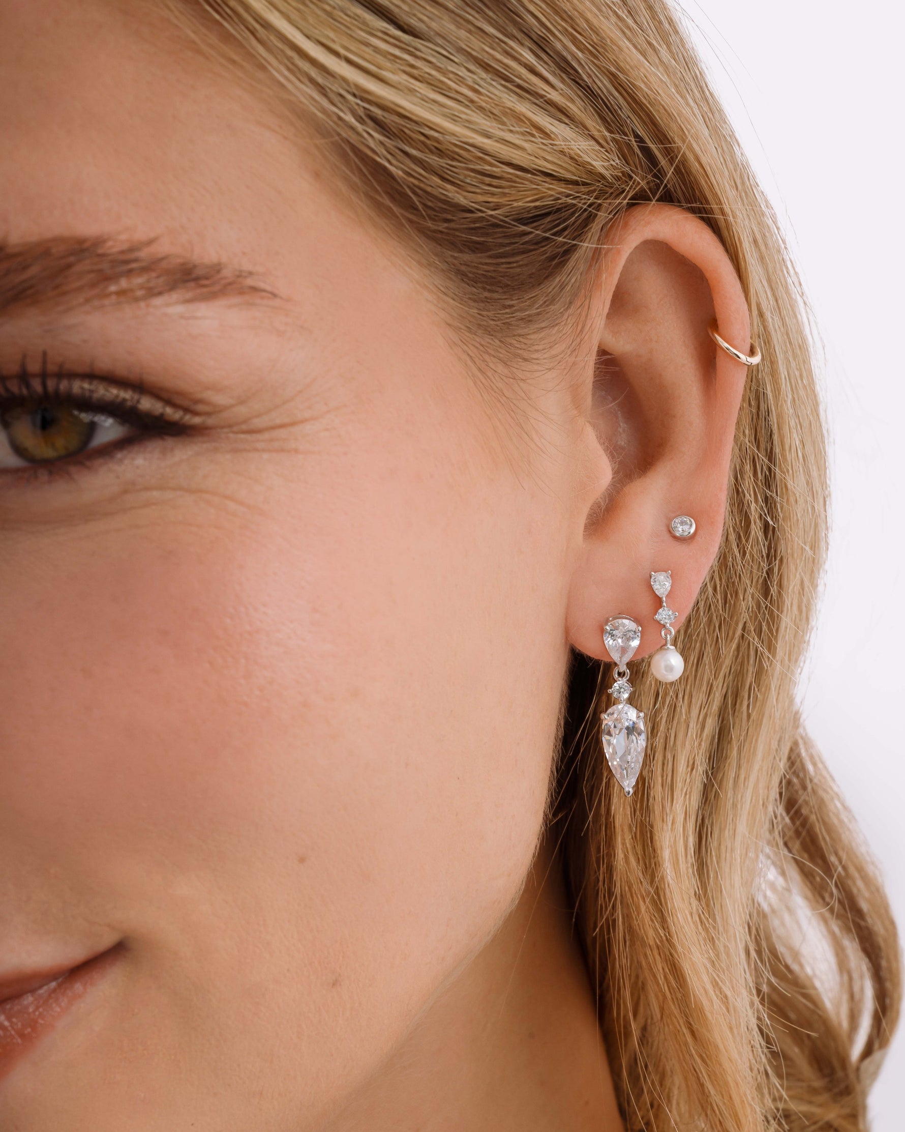 Sterling silver dangle earrings on model featuring a pear drop stud earring, a pearl drop earring, and a sterling silver stud earring