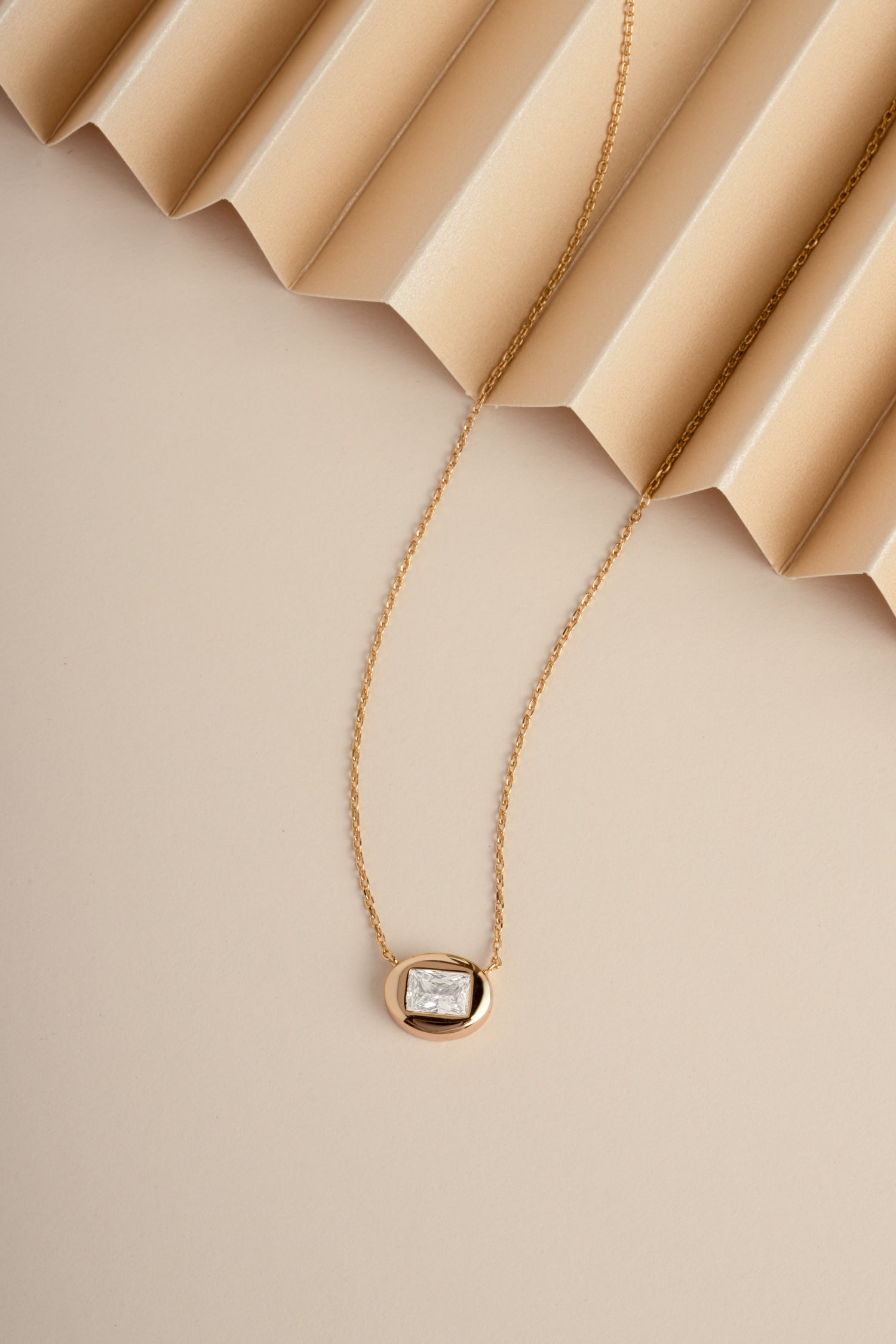 Dainty gold pendant necklace on beige textured background