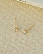 Gold tear drop diamond earrings with a push back closure style on a beige background