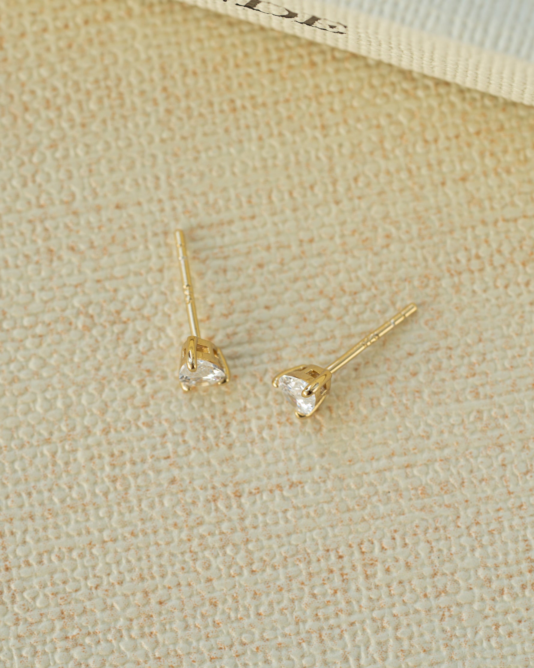 Gold tear drop diamond earrings with a push back closure style on a beige background