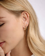 Model wearing gold huggie hoop earrings with a celestial jewelry inspired design, followed by dainty huggie hoops, and pear cut studs 