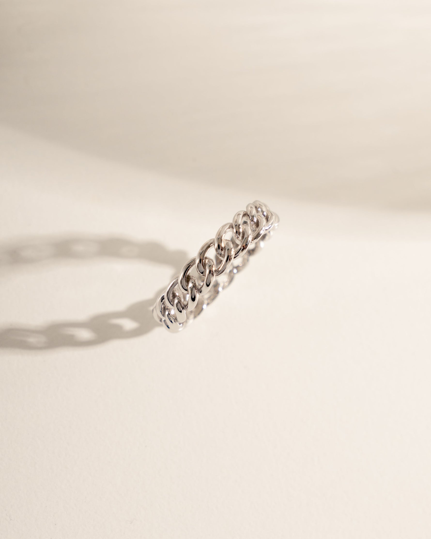 Silver ring with chain design on a light beige background