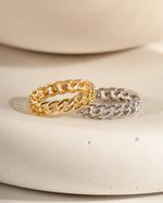 Two chain-link rings, one gold and one silver, on a neutral background