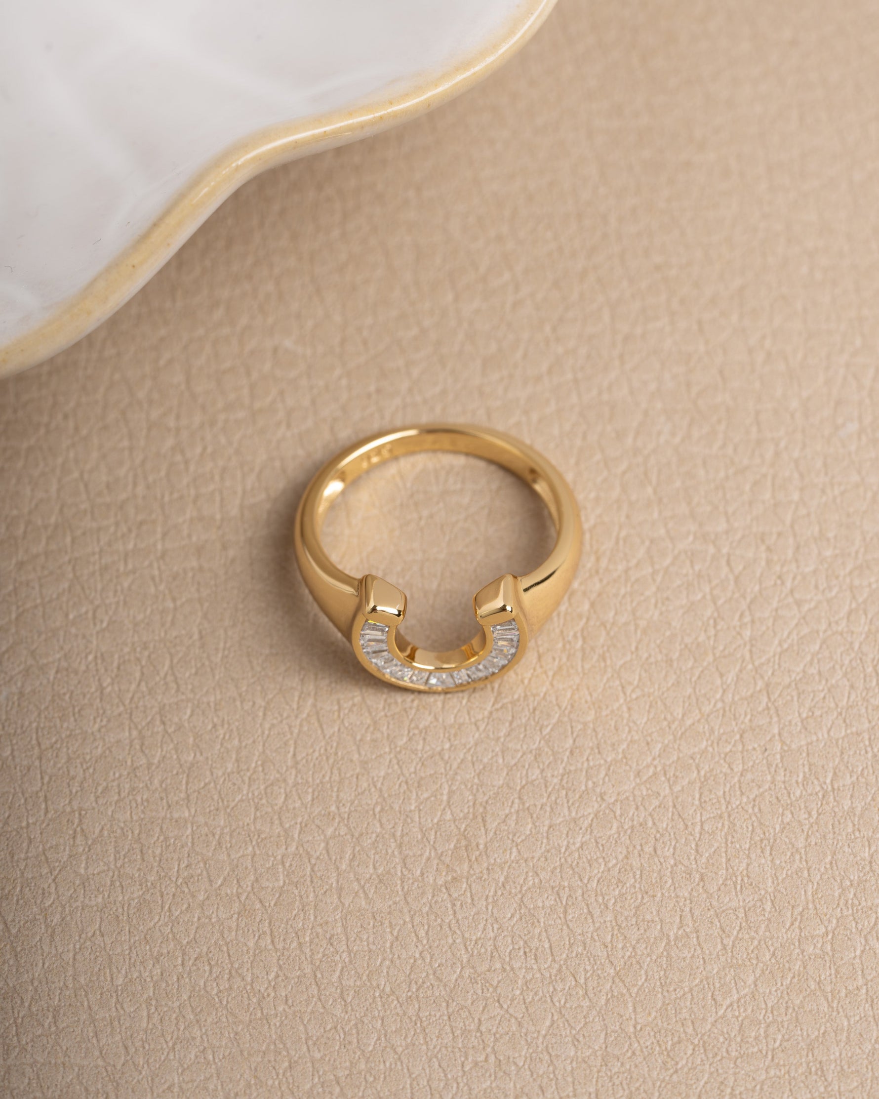 Chunky gold horseshoe ring on a plain background with a decorative plate