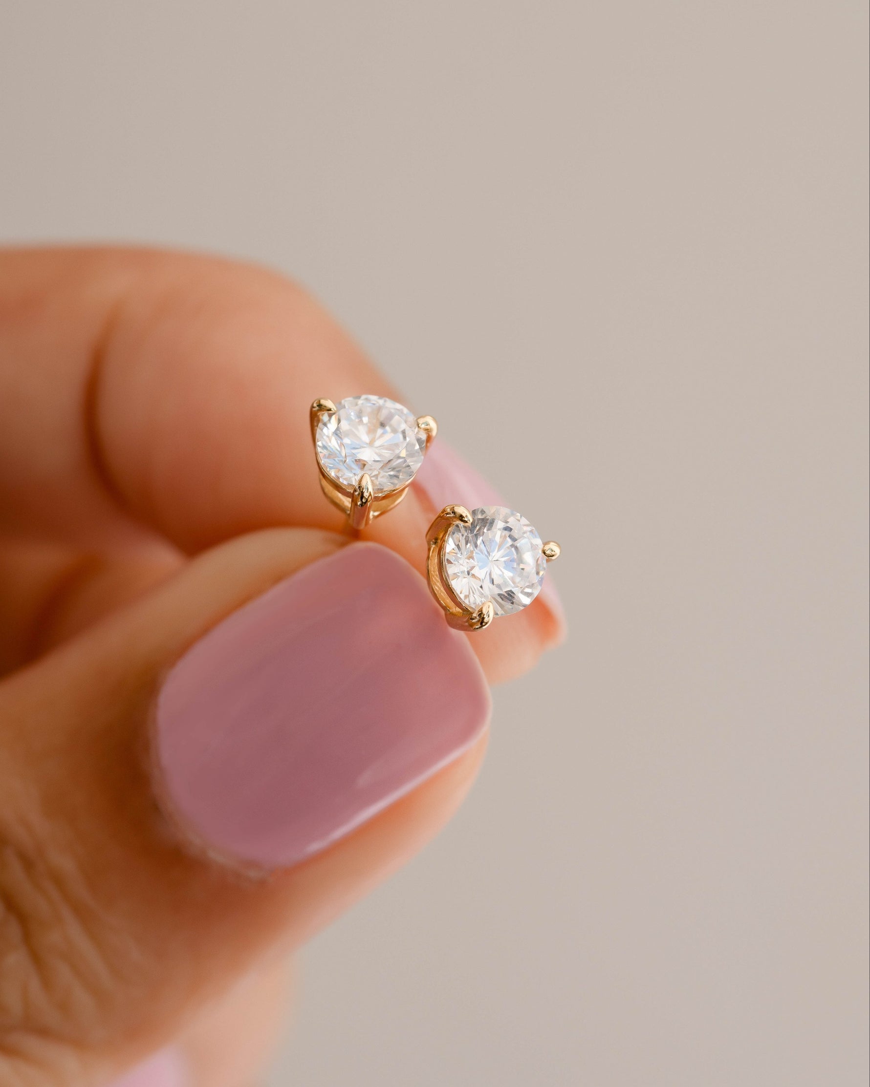 Gold studs being held in between two fingers