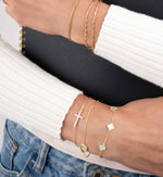 Model wearing gold bracelet stacks on each wrist while holding a spiral notebook, featuring a gold pearl bracelet, a gold chain bracelet and a gold cross pendant adjustable bracelet
