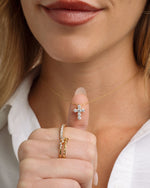 Model holding dainty cross pendant gold chain necklace with gold stackable rings