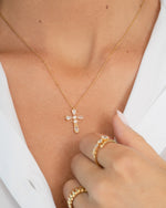 Gold cross necklace and gold statement rings on a person wearing a white shirt