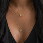 model wearing gold necklace stack including an oval medallion pendant necklace, a beaded chain necklace, and a small cross pendant necklace