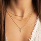 model wearing gold necklace stack featuring a cross pendant necklace, a beaded chain necklace, and a small paperclip chain necklace