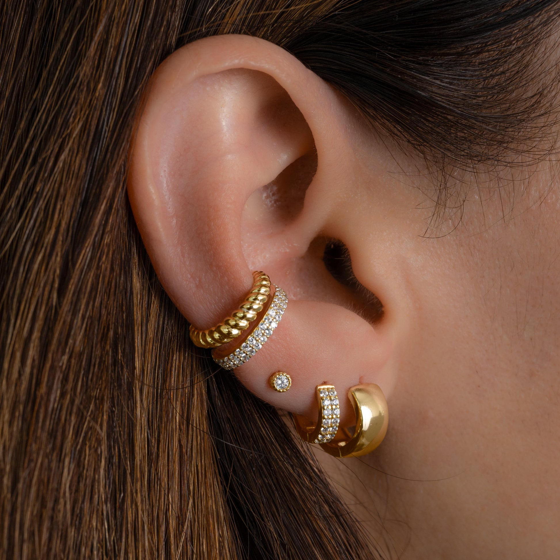 Model wearing gold earring stack featuring dainty cubic zirconia ear cuff