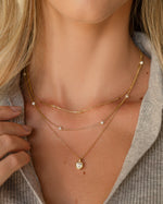 Model wearing gold layering necklaces featuring a gold chain necklace, a diamond beaded necklace, and a dainty pendant necklace