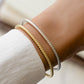 closeup image of model wearing two bangle bracelets with a twisted design in silver and in gold