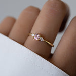 Gold ring with a pink gemstone on a finger against a white background