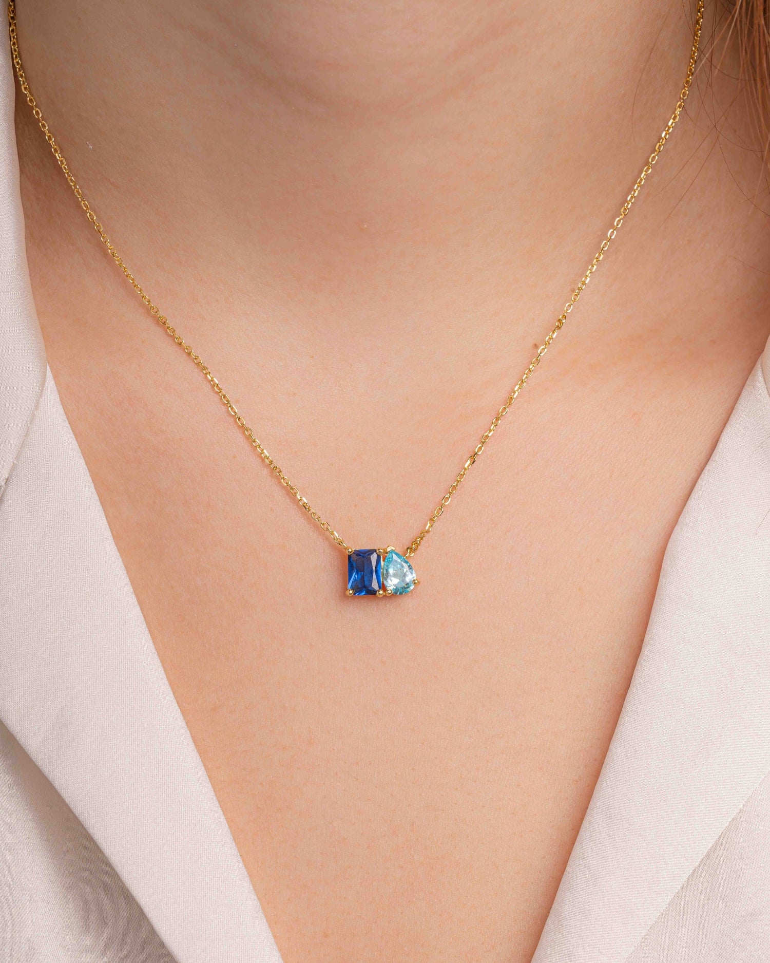 gold necklace with a pear cut sapphire birthstone and a emerald cut aquamarine birthstone