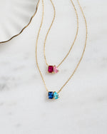 two gold toi et moi custom birthstone necklaces, featuring the ruby birthstone, rose quartz birthstone, aquamarine birthstone, and sapphire birthstone