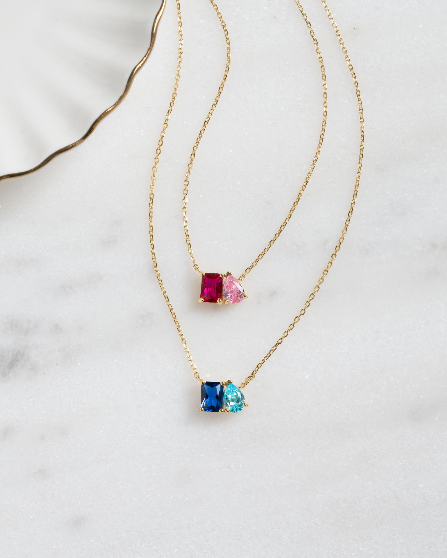 two gold toi et moi custom birthstone necklaces, featuring the ruby birthstone, rose quartz birthstone, aquamarine birthstone, and sapphire birthstone