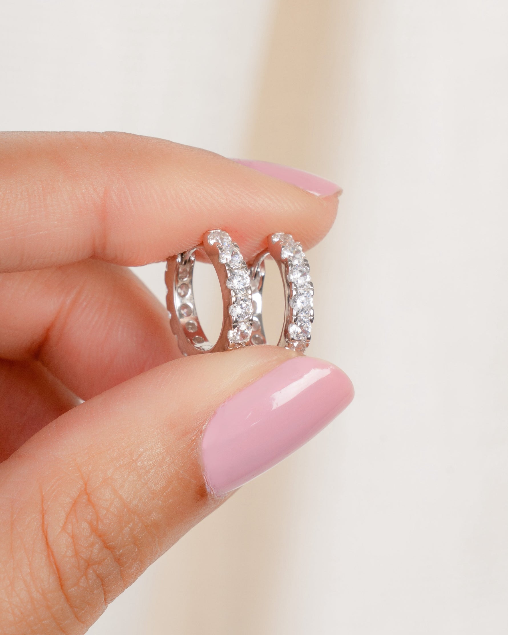 models hand holding silver cubic zirconia studded hoop earrings
