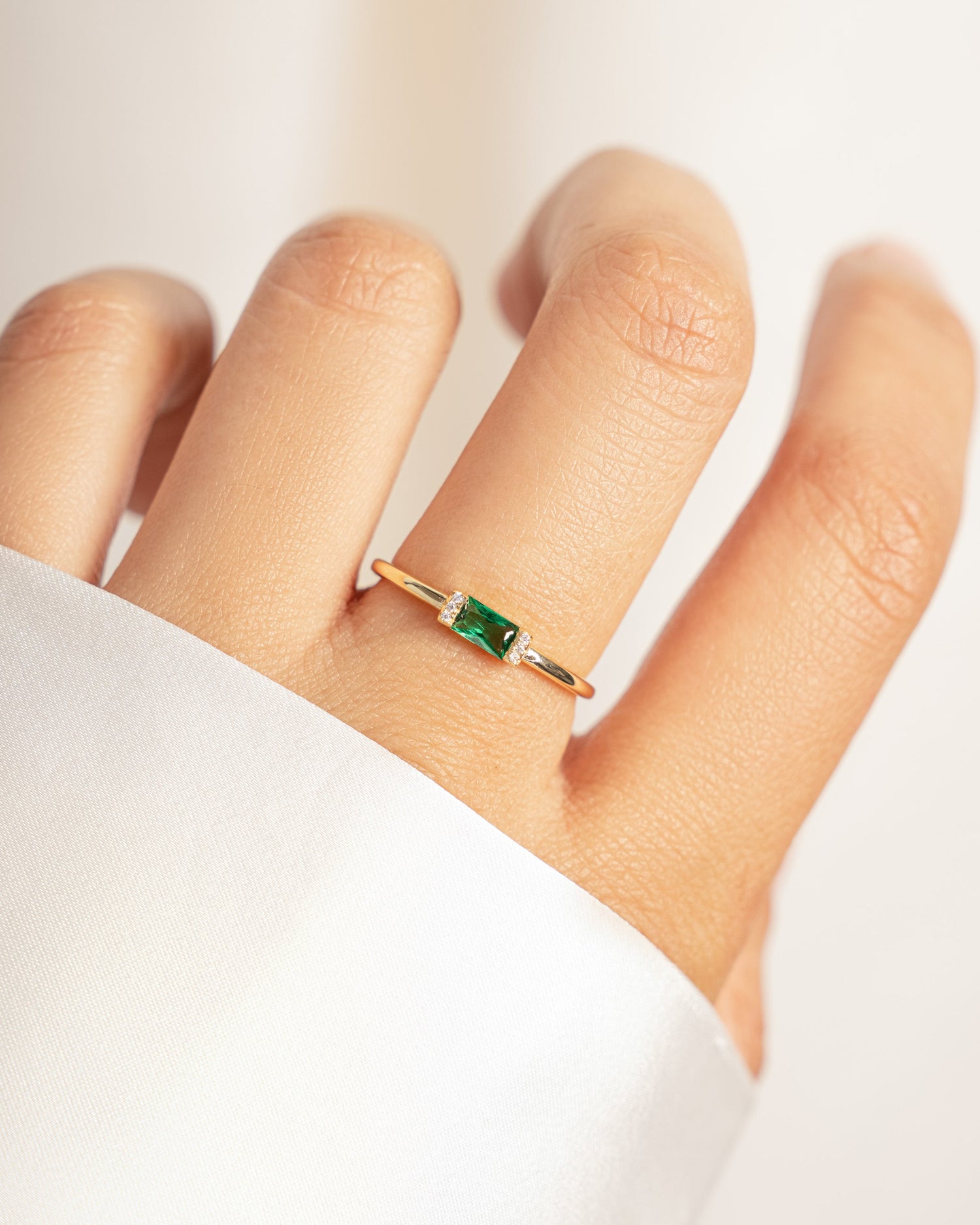 closeup image of models hands with emerald green baguette birthstone ring