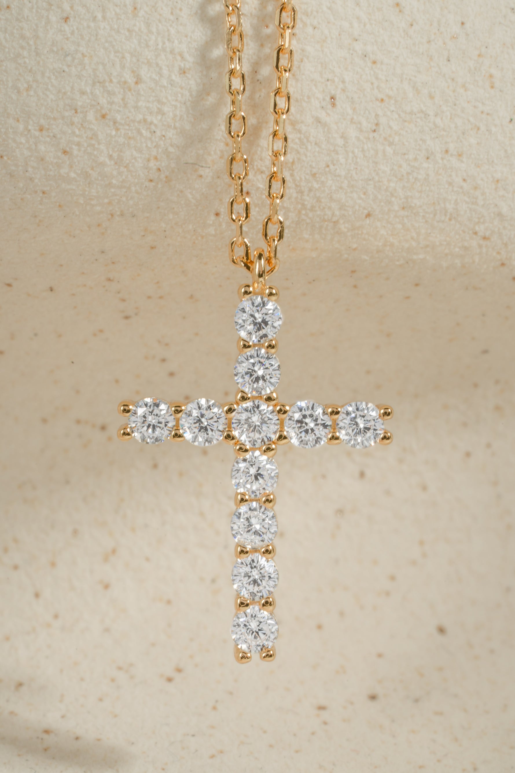 Gold chain necklace with diamond cross pendant on a beige background