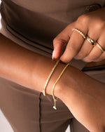 model wearing gold diamond cut bracelet and dainty baguette bracelet