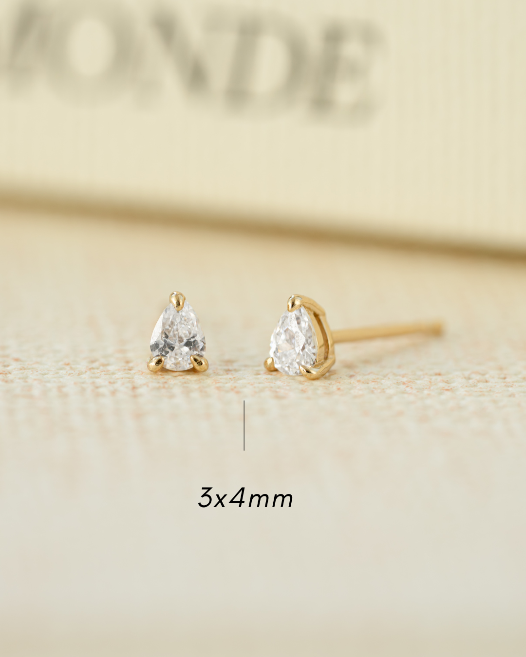 Pair of gold teardrop earrings on a beige background with '3x4 mm' text.