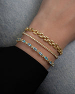 gold bracelet stack on model featuring a thick gold chain bracelet, a round tennis bracelet, and aquamarine tennis bracelet