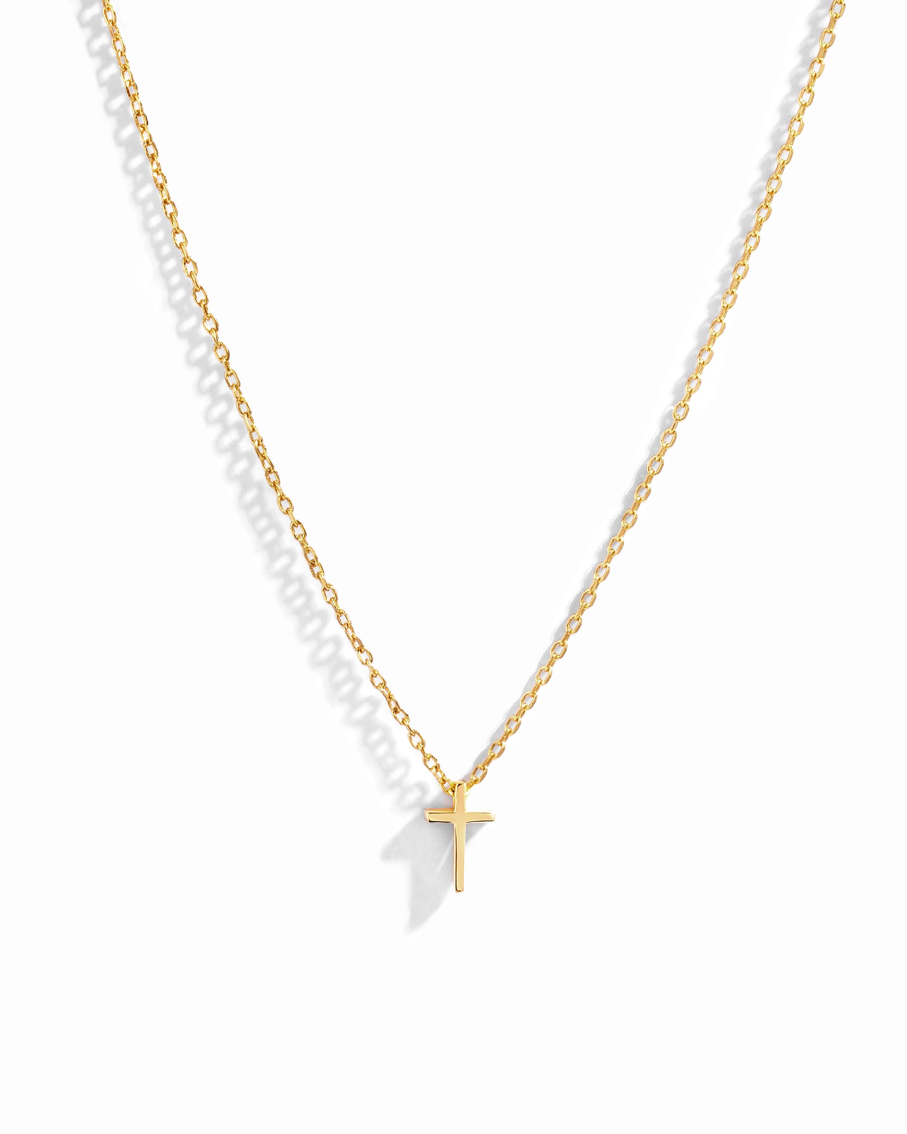 Dainty gold plain cross necklace on delicate chain on white background