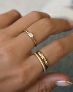 Hand wearing a baguette cut stacking ring, a celestial dome ring, and a cubic zirconia eternity ring. 
