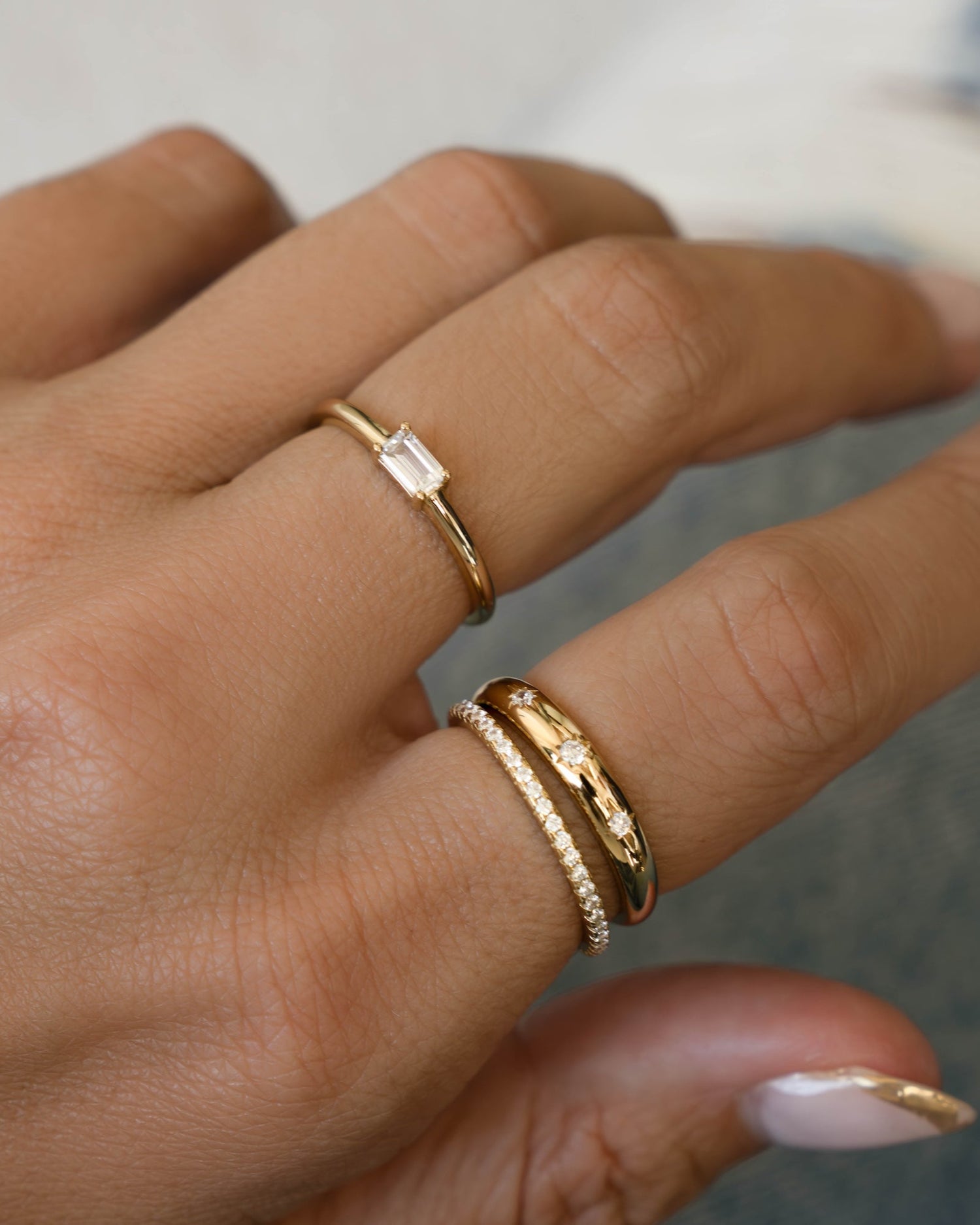 Hand wearing a baguette cut stacking ring, a celestial dome ring, and a cubic zirconia eternity ring. 
