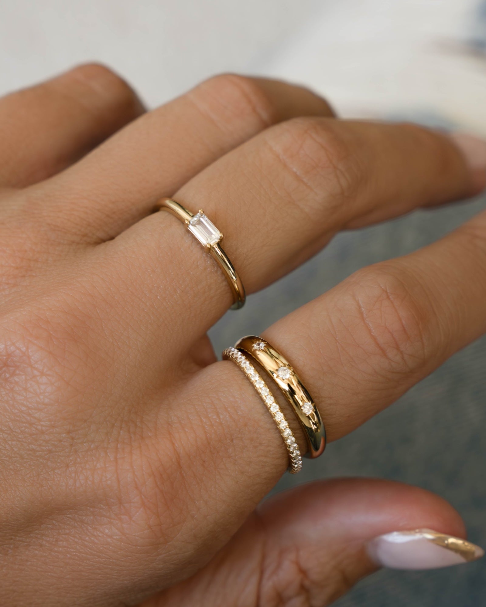 Hand wearing a baguette cut stacking ring, a celestial dome ring, and a cubic zirconia eternity ring. 
