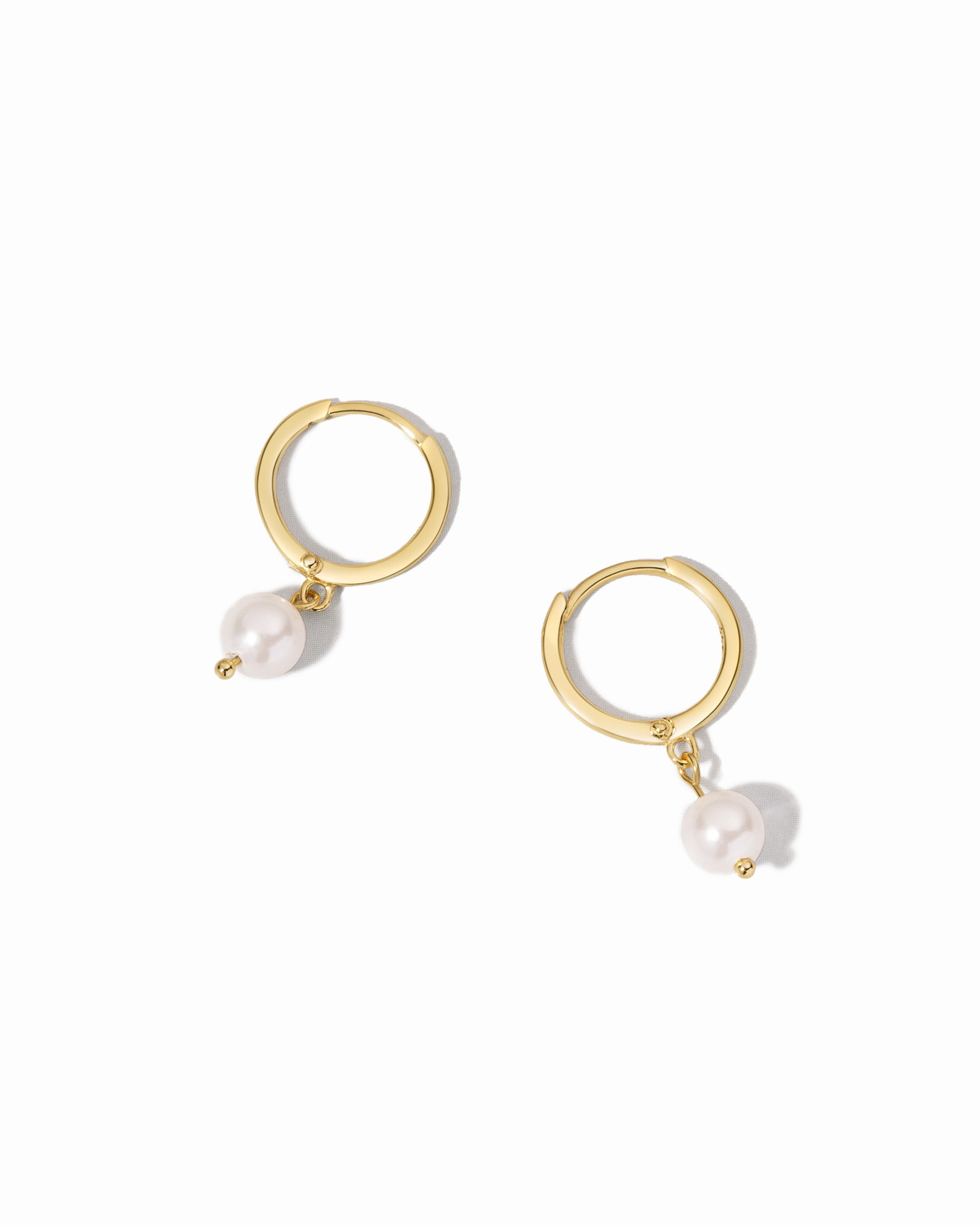 Gold hoop earrings with white pearls on a white background